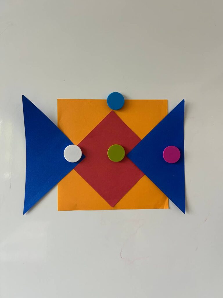 Farbige geometrische Papierformen liegen zu einer symmetrischen Anordnung auf einer hellen Fläche.